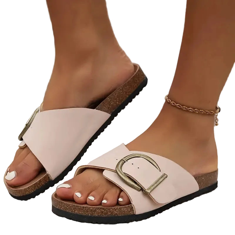 Pink sandals with gold buckles worn by a person on a blurred outdoor background