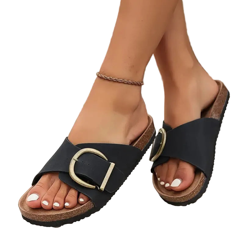 Black sandals with gold buckles worn by a person on a blurred natural background